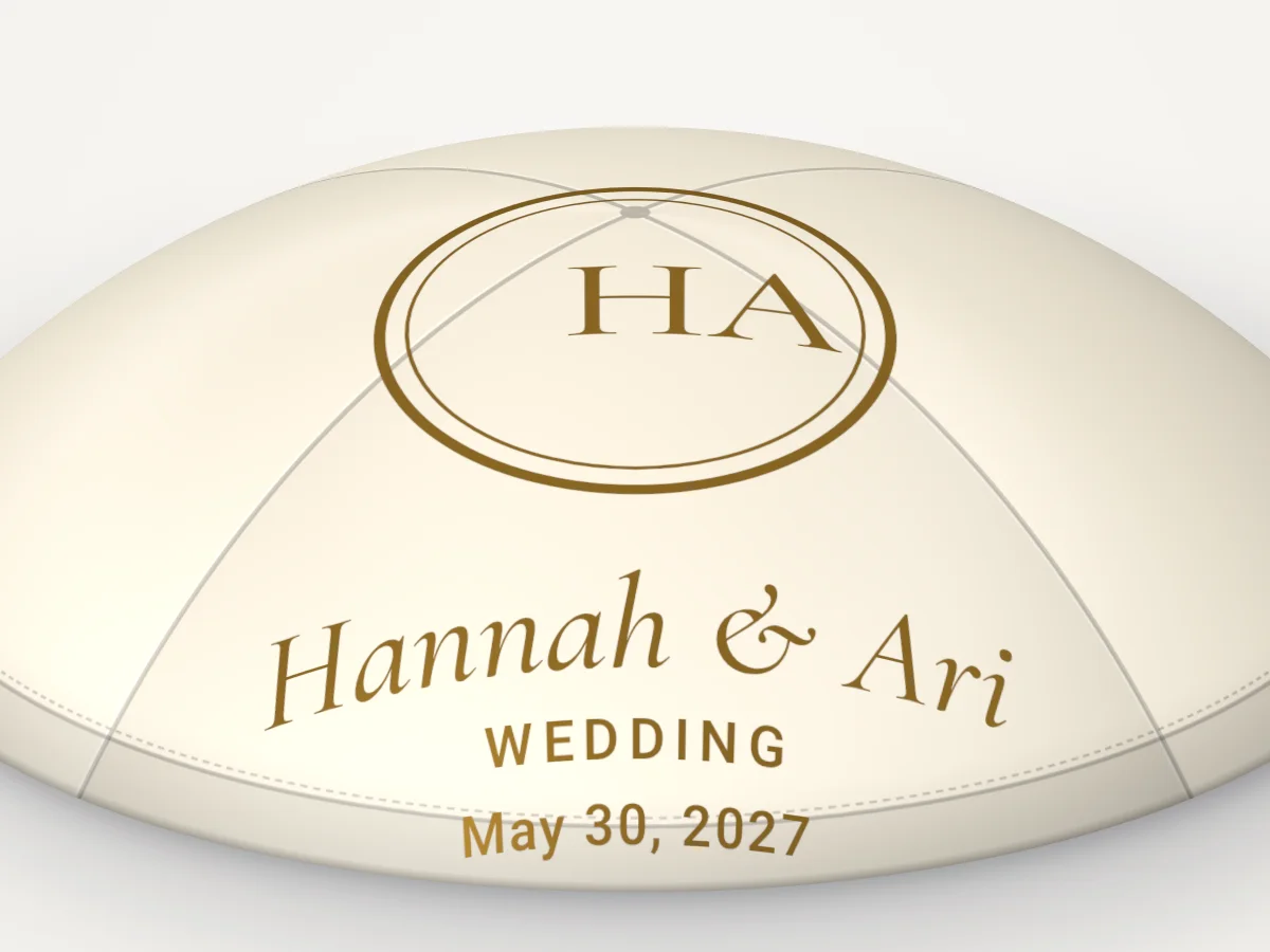 Close view of an ivory satin kippah with a gold monogram and the names Hannah and Ari